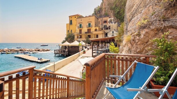 A coastal hotel with a wooden deck, lounge chairs, and a view of the sea and rocky cliffs. - Casa della Marina · Historic beachfront tonnara with direct sea access (Conca dei Marini)