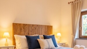 A bed with striped bedding, two bedside tables with lamps, a wooden headboard, and a window with curtains. - Casa della Marina · Historic beachfront tonnara with direct sea access (Conca dei Marini)