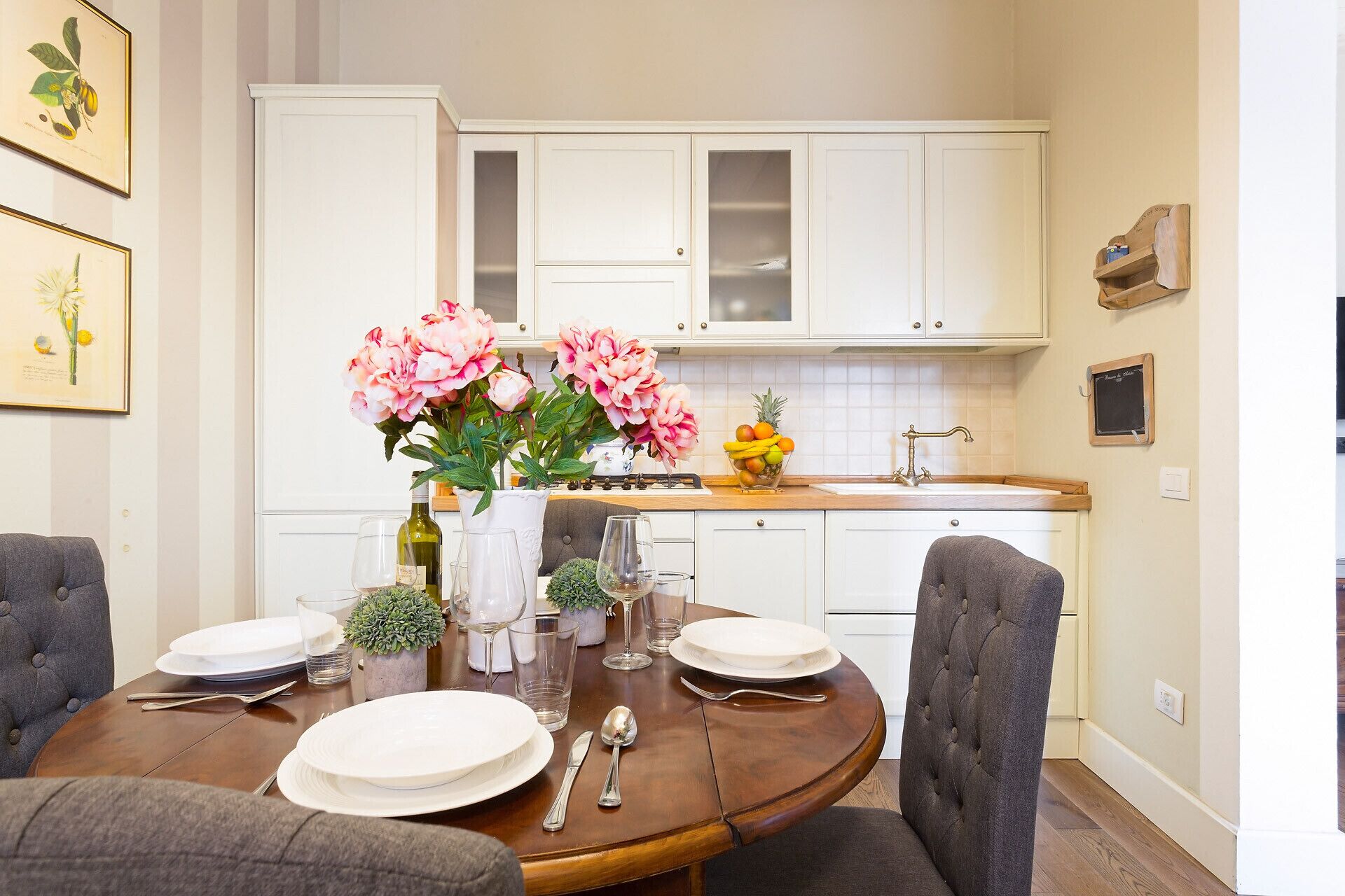 A dining area with a round table set for four, white cabinets, and a kitchen in the background.