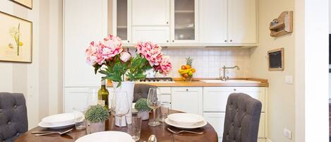 A dining area with a round table set for four, white cabinets, and a kitchen in the background.