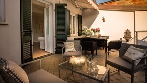 Un espace extérieur aménagé en terrasse, avec une table à manger, des chaises et un canapé. On y trouve une table en verre ornée d’une bougie et de fleurs.
