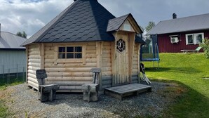 Une petite cabane en bois, dotée d’un toit à forte pente, d’une cheminée et d’un petit porche avec des bancs.
