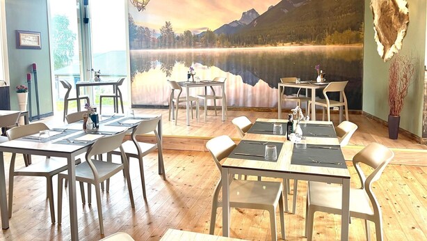 Un espace repas avec des tables et des chaises en bois, une fresque représentant un lac et des montagnes, et des luminaires suspendus.