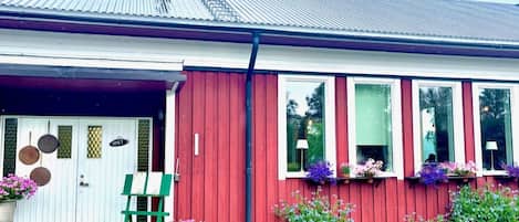 A red building with a white door, windows with flower boxes, and a green chair outside.