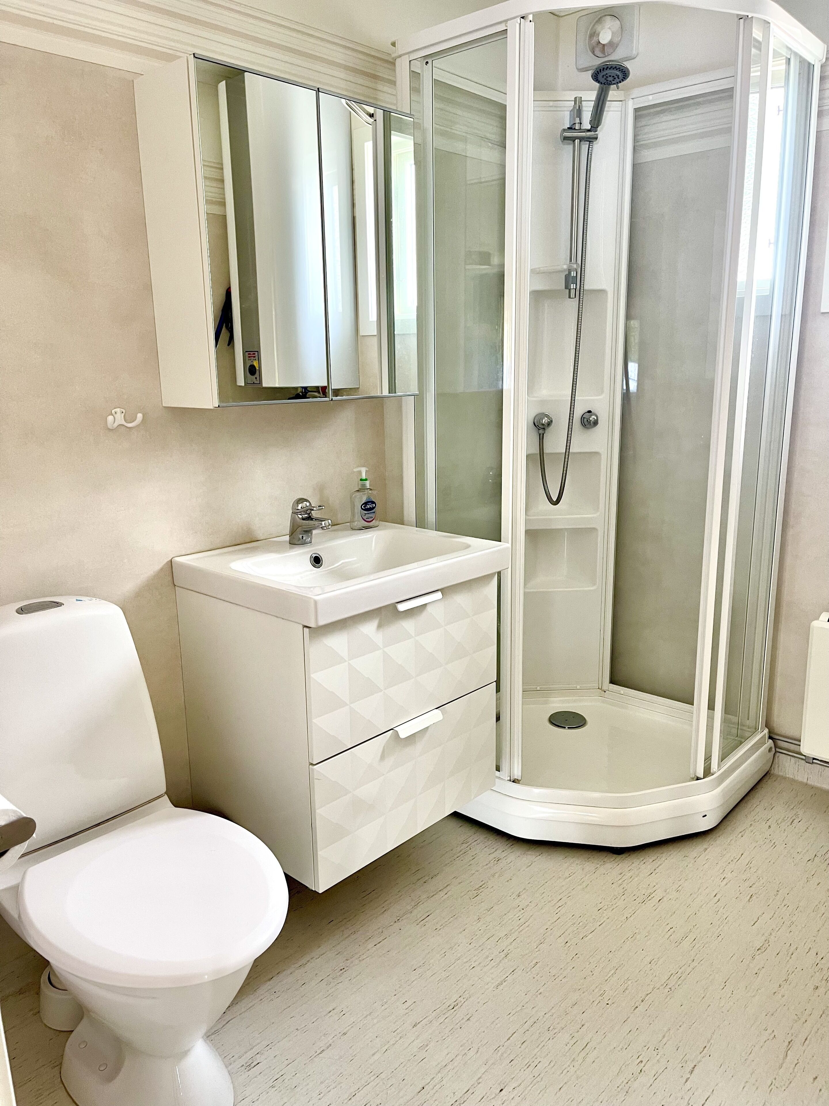 Un baño moderno con inodoro, lavabo con espejo y ducha con mampara de vidrio.
