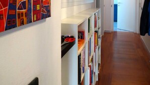 A hallway with white shelves, a colorful painting of a tree and houses, and a door leading to a kitchen. - Bright, spacious, terraces, one step from the sea, high-speed wifi, Cinqueterre (Sestri Levante)