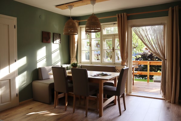 Un coin repas avec une table et des chaises en bois, un banc et une vue sur un jardin grâce à de grandes fenêtres.