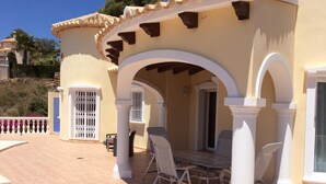 A covered outdoor patio with a table and chairs, white columns, and a tiled floor.