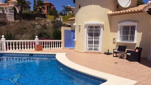A swimming pool with a tiled edge, a white gate, and outdoor furniture.