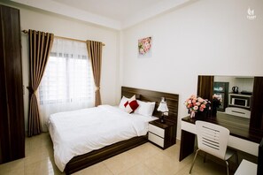 A hotel room with a bed, bedside tables, a desk with a chair, a mirror, a microwave, and a floral arrangement. - KorHan Apartment (Hanoi)