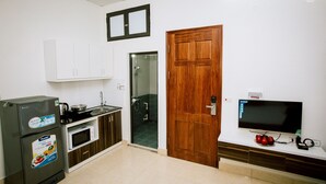 A compact kitchen with a refrigerator, microwave, stove, and a television on a stand. - KorHan Apartment (Hanoi)