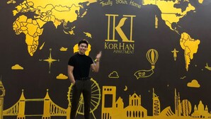 A man standing in front of a wall with a world map and the text "KORHAN APARTMENT" and "Truly Your Home". - KorHan Apartment (Hanoi)