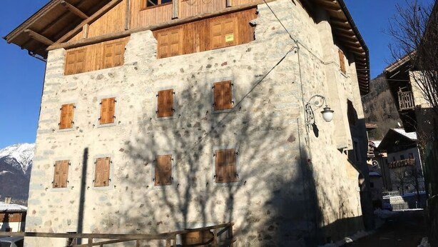 Ein mehrstöckiges Steinhaus mit Holzhinterfenstern, einem Balkon und einem Berg im Hintergrund.