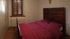 Ein Schlafzimmer mit einem hölzernen Bett, einem Fenster mit Ausblick und einer Heizkörper.