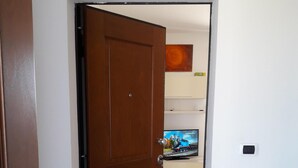 A wooden door leading to a room with a tiled floor, a television, and a small shelf with items on it.