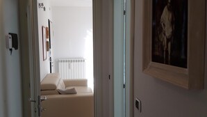 A hallway leading to a bedroom with a bed, a painting on the wall, and a door.