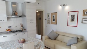 A modern kitchen with white cabinets, a dining table with a floral tablecloth, and a beige sofa with cushions.