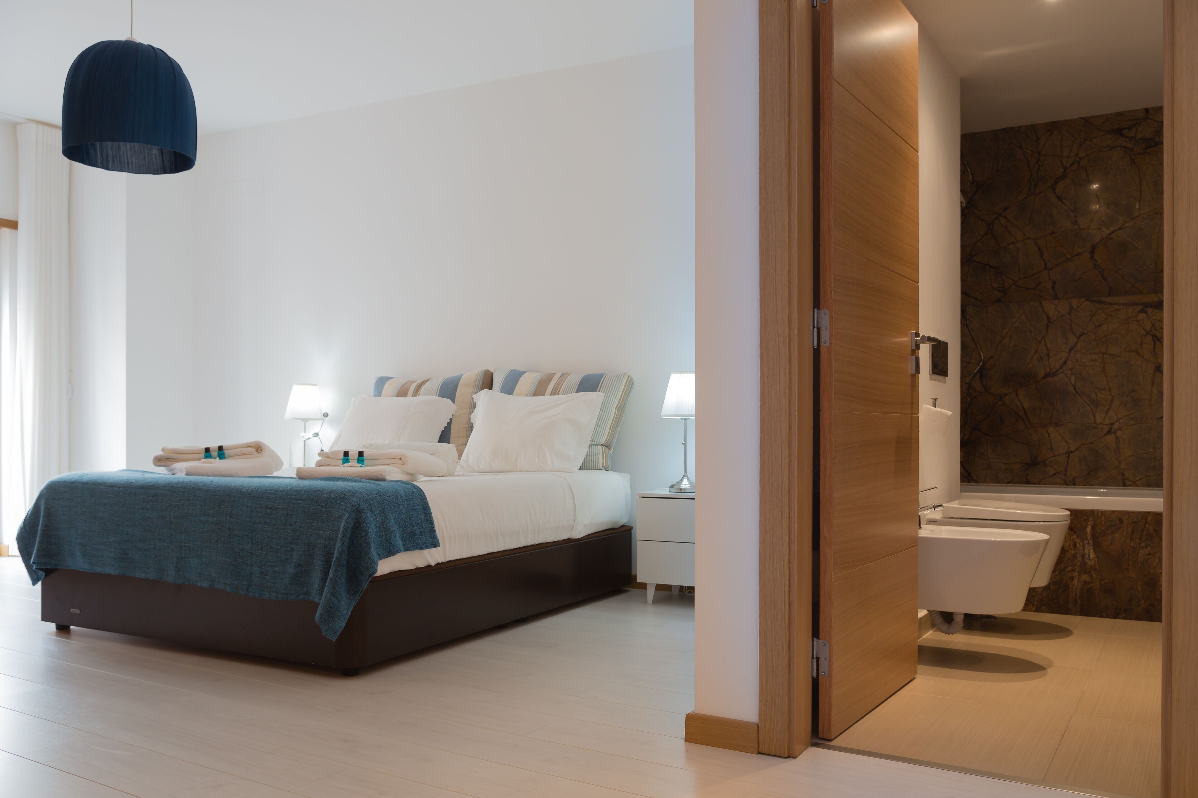 A modern bedroom with a bed, bedside tables, and a bathroom with a toilet and sink.