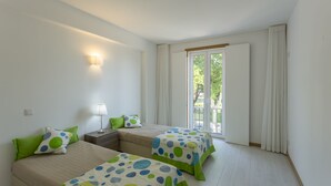 A room with two beds, a nightstand, a lamp, and a sliding glass door leading to an outdoor area. - 3 BEDROOM APARTMENT IN THE CENTER OLHAO (Olhão)