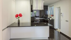 A modern kitchen with a black countertop, stainless steel range hood, and a vase with red flowers. - 3 BEDROOM APARTMENT IN THE CENTER OLHAO (Olhão)