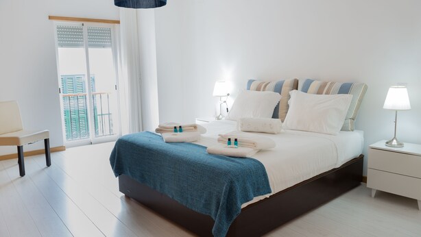 A modern bedroom with a large bed, bedside tables, a bench, and a view of the outside. - 3 BEDROOM APARTMENT IN THE CENTER OLHAO (Olhão)