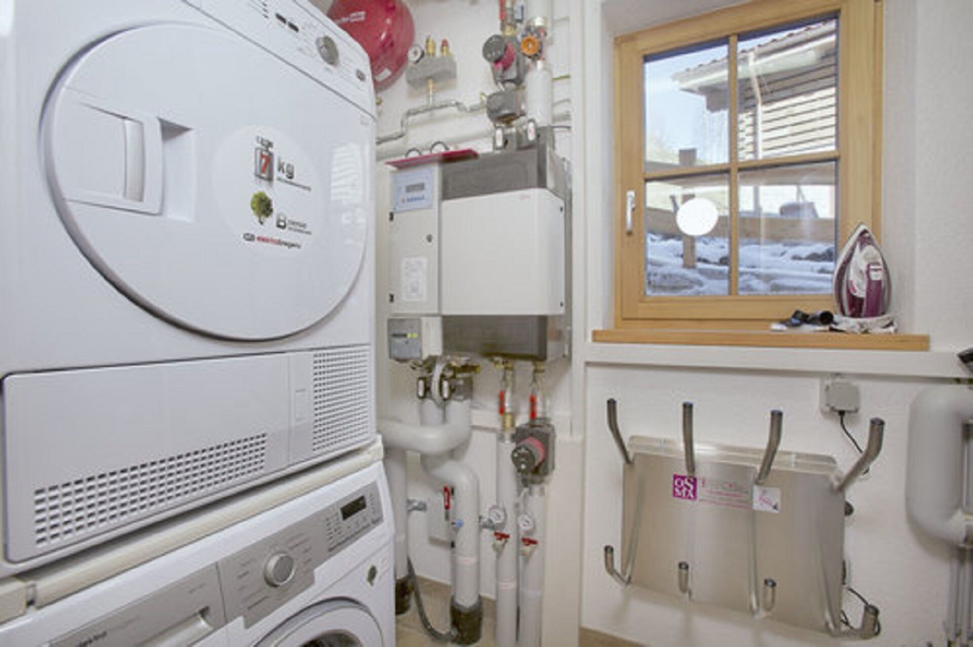 A laundry area with a washing machine, dryer, and water heater. There are pipes and a window with a view of the outside.