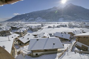 Een dorp bedekt met sneeuw, met traditionele houten huizen, een berg op de achtergrond en een heldere lucht.
