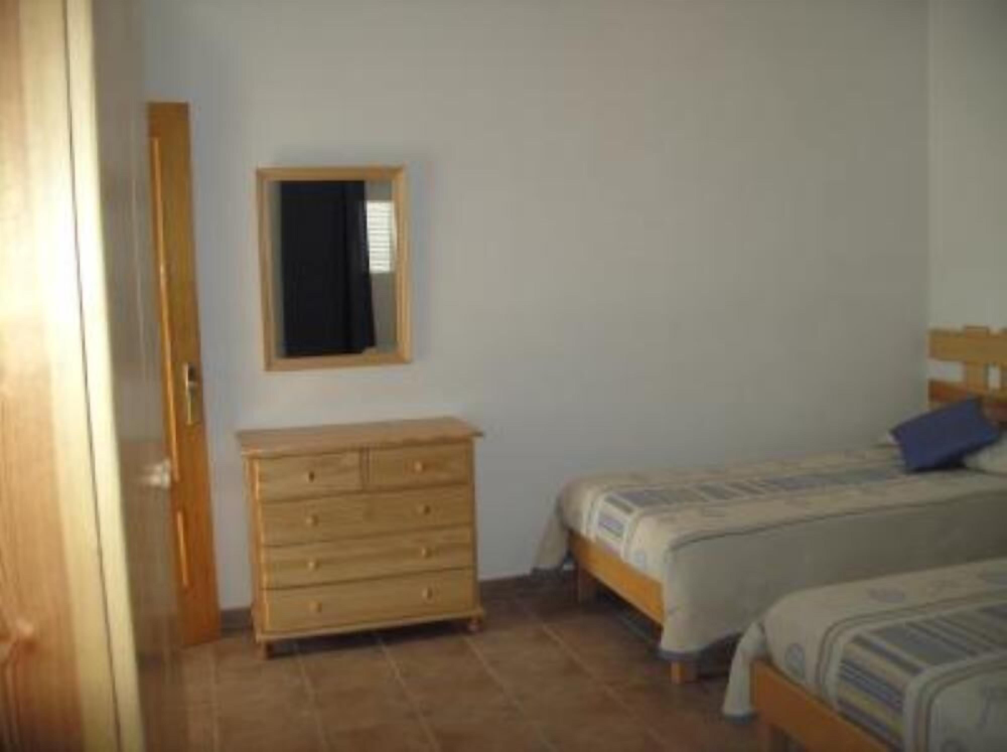 A bedroom with two beds, a wooden dresser, and a mirror on the wall.