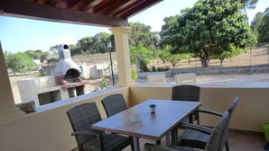 Une terrasse extérieure avec une table et des chaises en osier, donnant sur un jardin et un four en briques.
