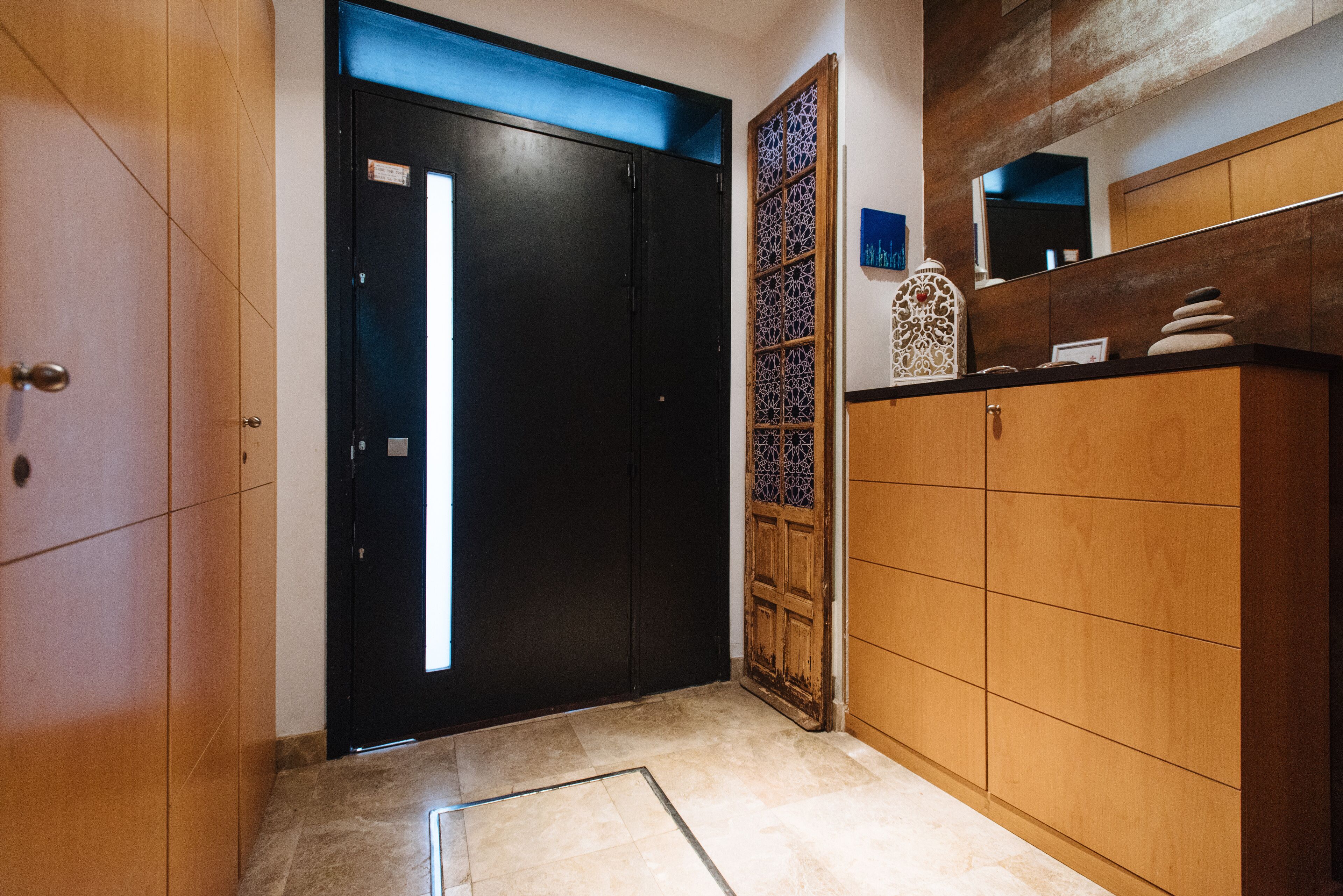 A hallway with a black door, wooden cabinets, and a decorative wall panel.