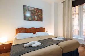 A neatly made bed with white linens and towels, a wooden headboard, a quilt, and a wall-mounted artwork.