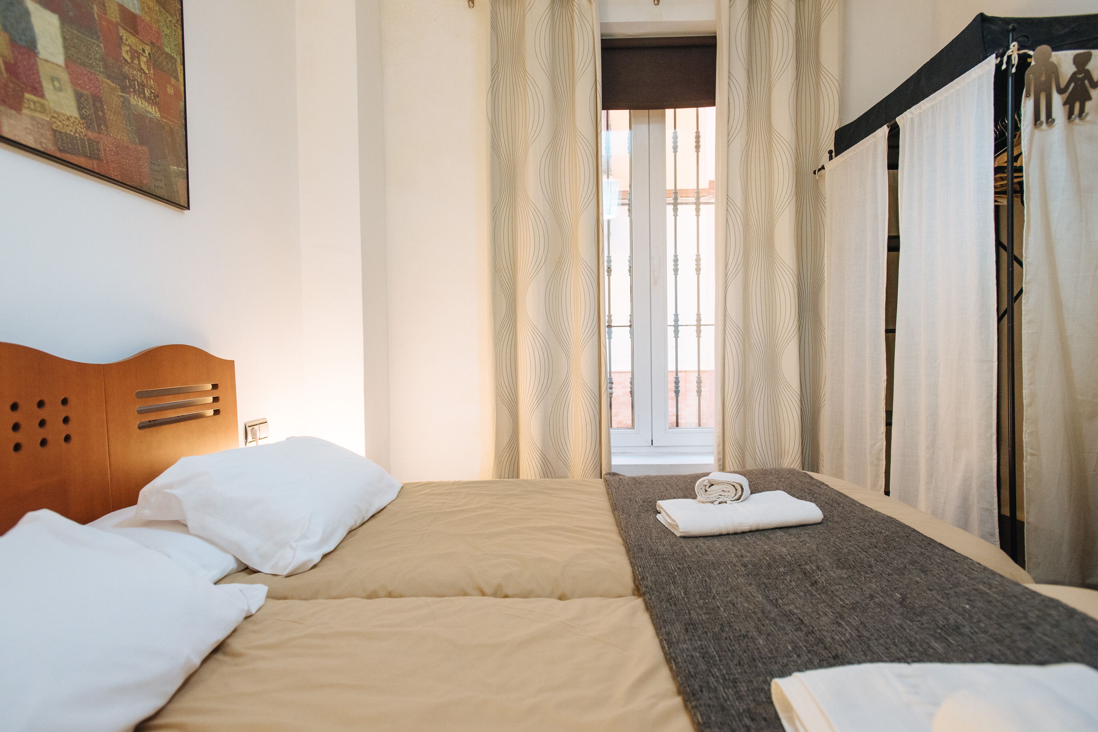 A hotel room with a bed, a wooden headboard, a window with curtains, and a view of the outside.