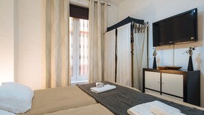 A hotel room with a bed, a TV, a small table, and a window with curtains.