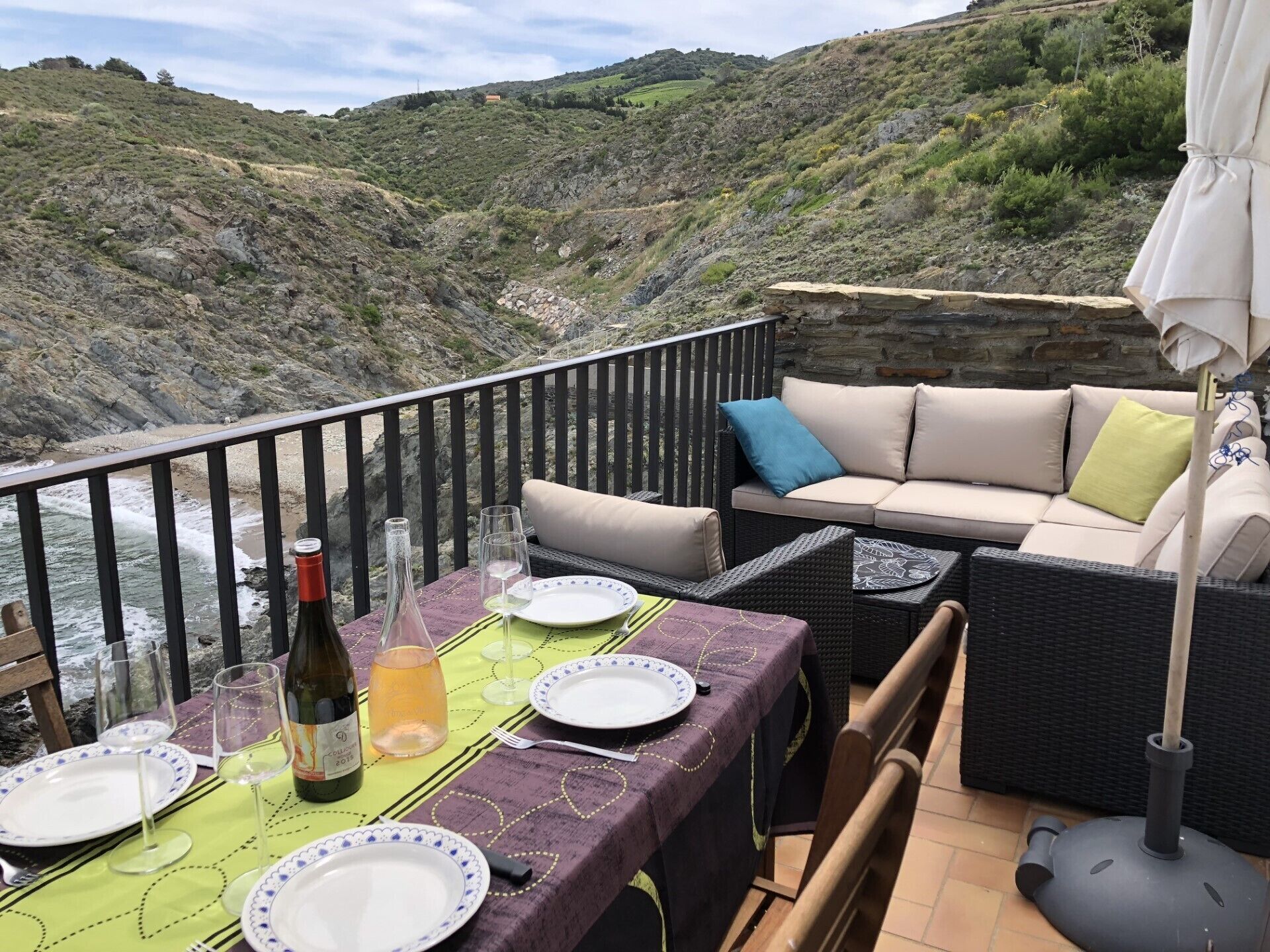 A dining area with a table set for two, overlooking a rocky hillside and the sea.
