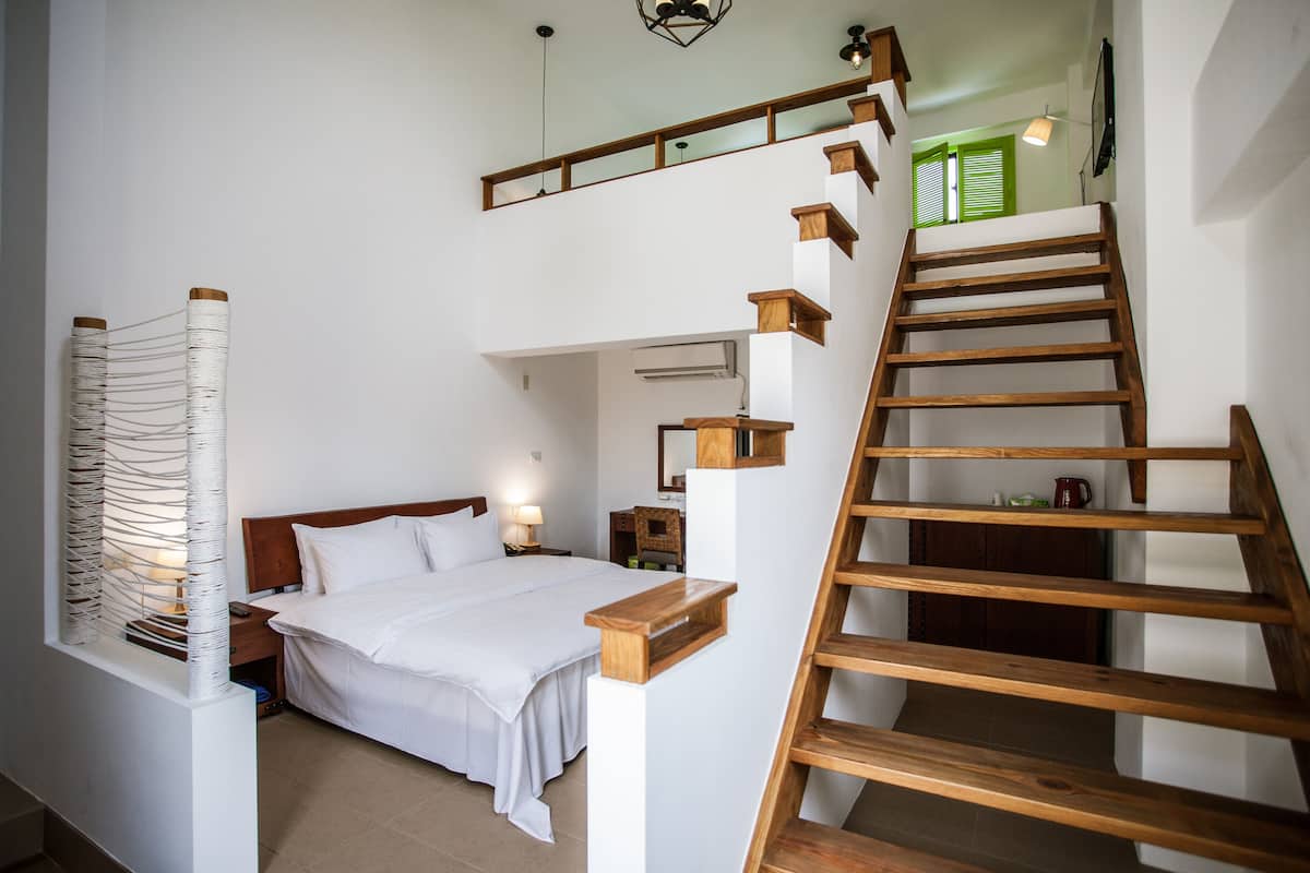 Un dormitorio con cama, escalera de madera y una escalera que sube a un nivel superior.