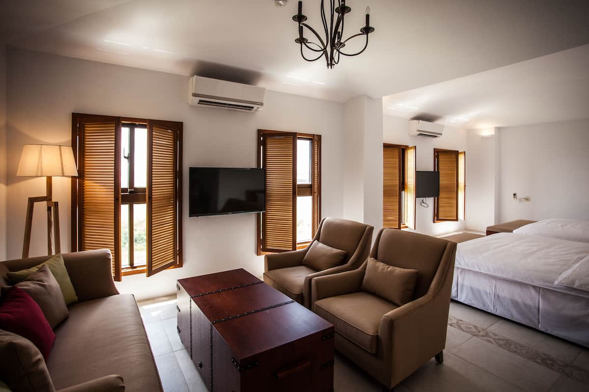 Una habitación de hotel moderna con sofá, sillón, mesita de noche y cama.