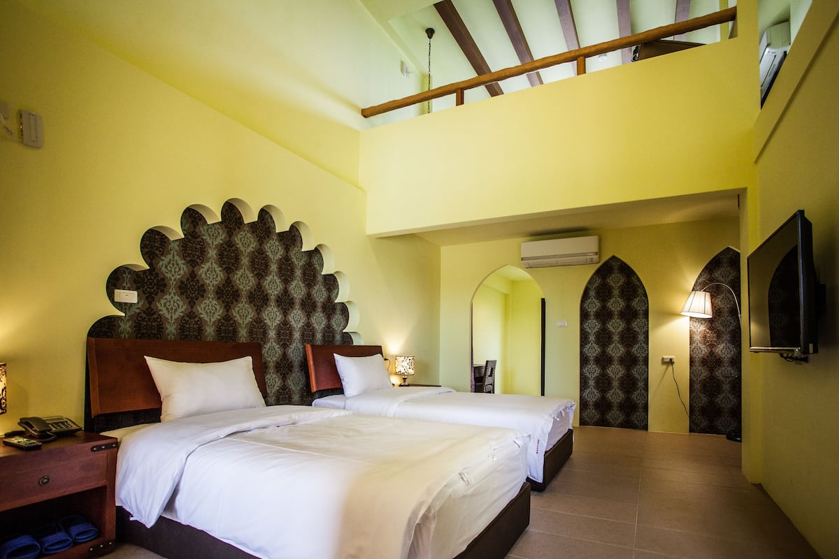 Habitación de hotel con dos camas, cabecera de madera, televisor de pantalla plana y balcón.