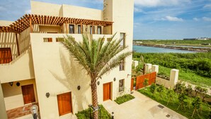 Un edificio moderno con varias puertas y ventanas, una palmera en el patio y vista al mar.