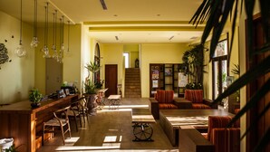 Un amplio vestíbulo de hotel con un mostrador de recepción de madera, varias zonas de estar y una escalera que conduce a un piso superior.