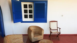 A room with wicker furniture, a wooden chair, and a window with blue shutters.