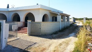 A two-story building with a covered porch, a gated entrance, and a dirt path leading to a vehicle.