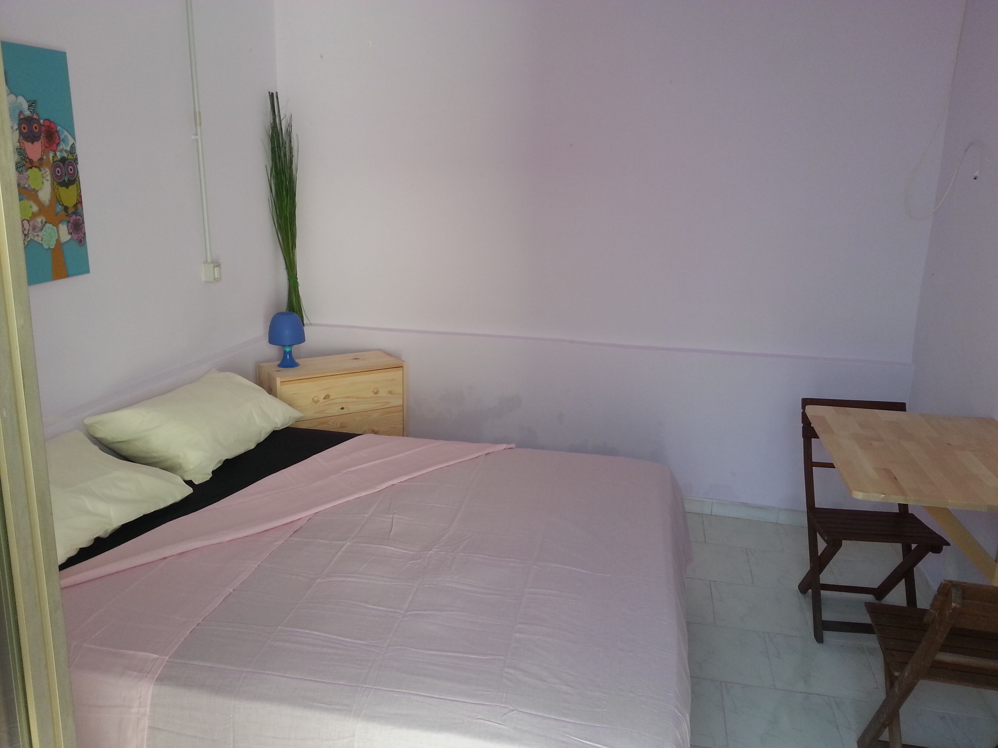 A bedroom with a bed, a nightstand, a lamp, a table, and a chair.