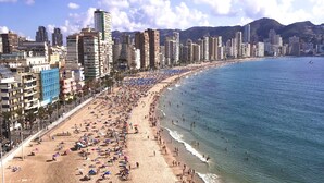 A beach with a cityscape in the background, including tall buildings and mountains.