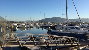 Puerto deportivo con barcos amarrados, cielo despejado y montañas al fondo.