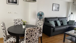 Una sala de estar moderna con una mesa redonda para comer, sillas con estampado floral, un sofá negro con cojines turquesa y una lámpara colgante negra.