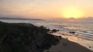 Una playa con terreno rocoso y vista al atardecer.