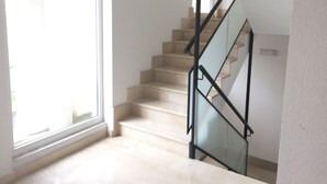 Una escalera con barandillas de cristal y peldaños color beige que sube a un piso superior.