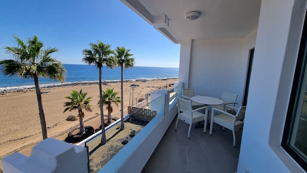 Un balcón con vista a la playa, muebles de mimbre blanco y barandilla.