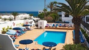 Una piscina en la azotea con sillas de descanso y sombrillas, con vistas a una playa y el océano.