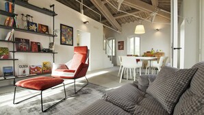 A spacious living area with a high ceiling, exposed wooden beams, a red armchair, a grey sofa, and a dining area with white chairs. - For those who love to pause in history and stories (Assisi)